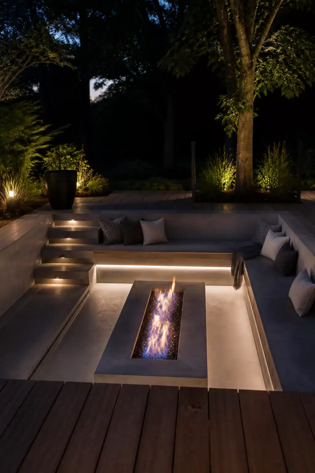 Sunken outdoor fire pit with blue gas flame, LED strip bench lighting and recessed seating at night.