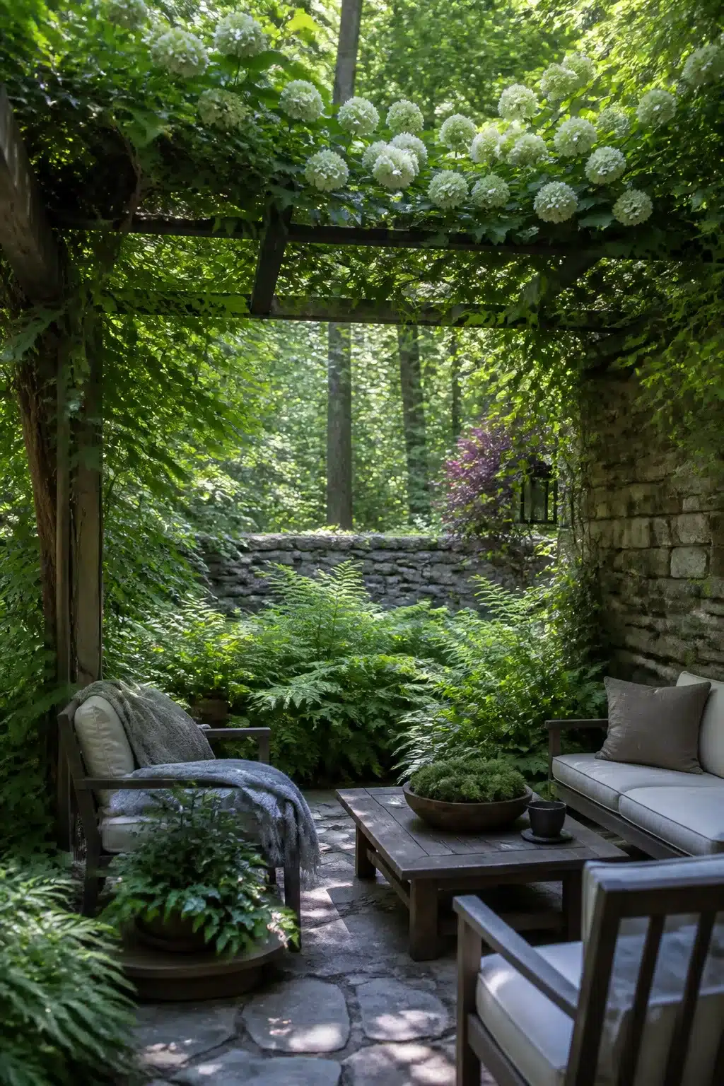White hydrangea pergola over a shaded stone seating area in a lush woodland courtyard garden with ferns