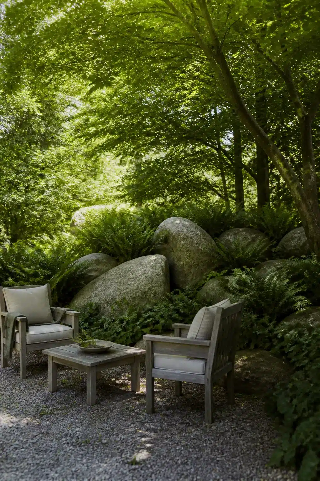 Granite boulders with fern groundcover in a shaded woodland rockery garden seating area with gravel floor