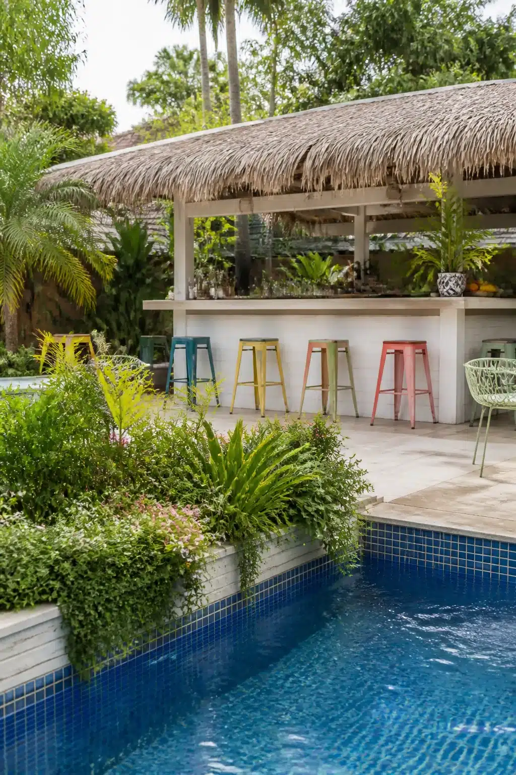 Tropical backyard bar ideas with thatched roof, colorful metal stools, and pool-side planter beds