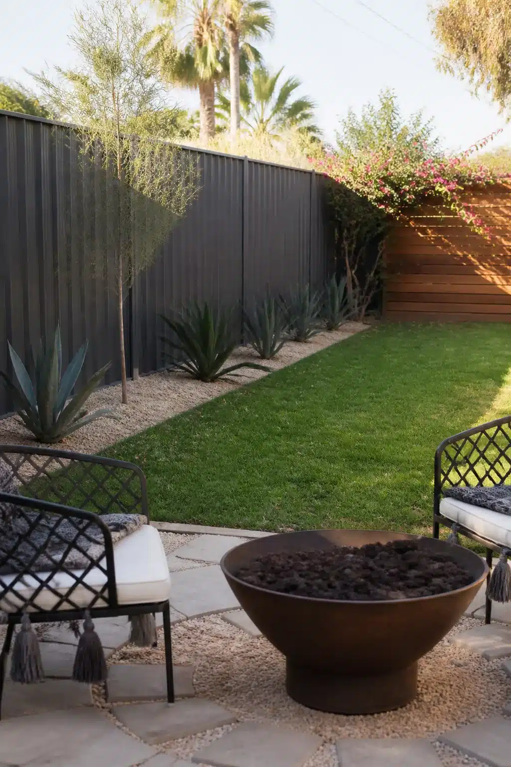 Dark metal fence with gravel strip and agave plants — backyard fence landscaping ideas for dry climates