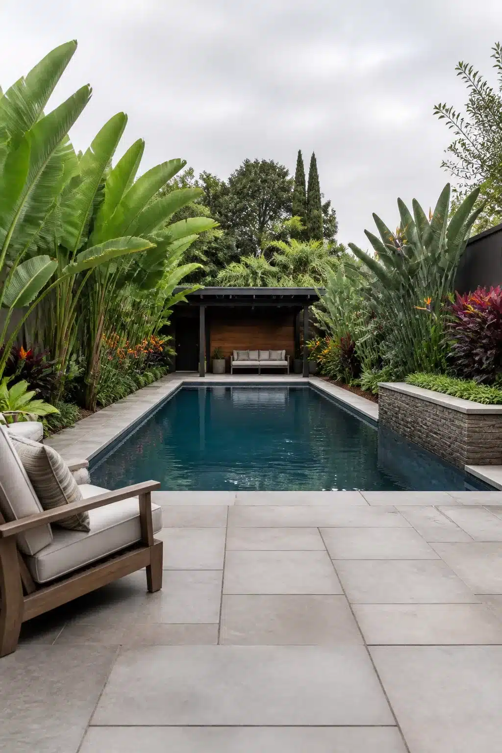 Tropical backyard landscaping design with dark pool, banana palms, and large concrete pavers surrounding a lush poolside garden.