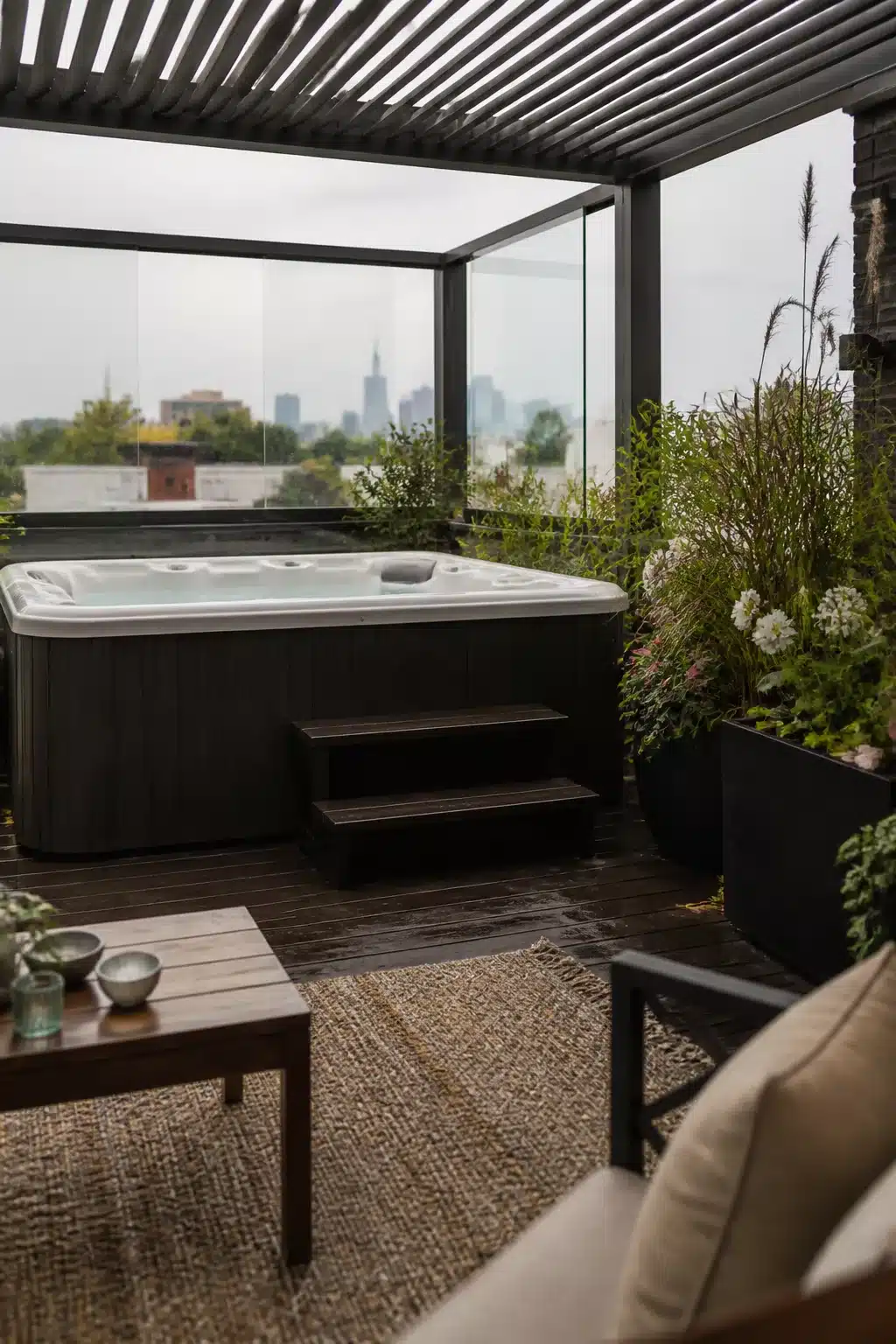 Enclosed hot tub ideas for backyards — dark steel pergola with glass panels on a city rooftop terrace
