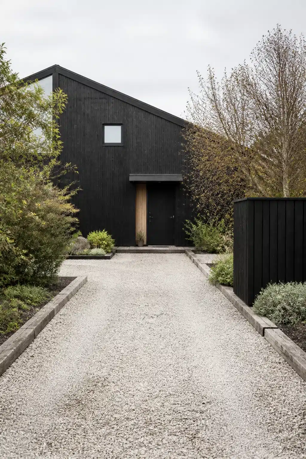 White gravel driveway ideas with black timber house facade and concrete edging for a Scandinavian-inspired approach