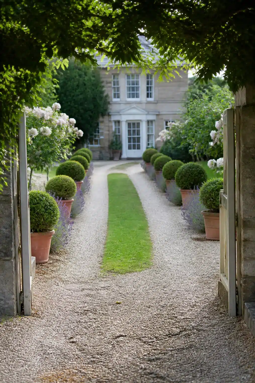 Formal gravel driveway ideas with twin tracks, grass runner, clipped box balls in terracotta pots and a country house backdrop.