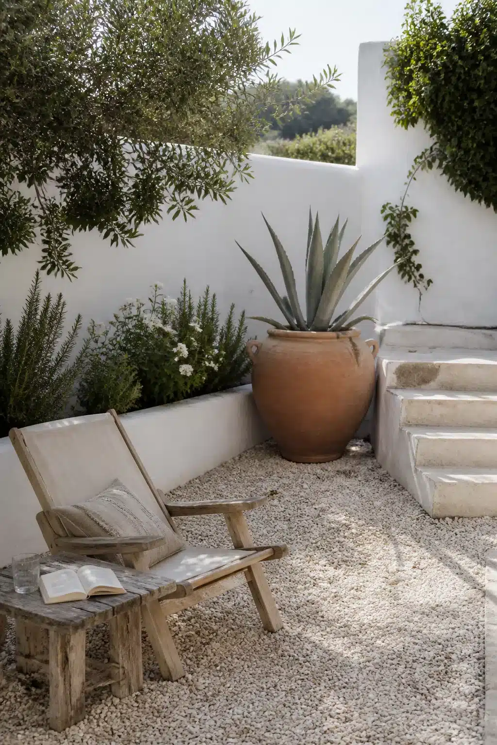 Minimalist Mediterranean garden courtyard with gravel floor, terracotta urn, agave plant, and whitewashed walls.