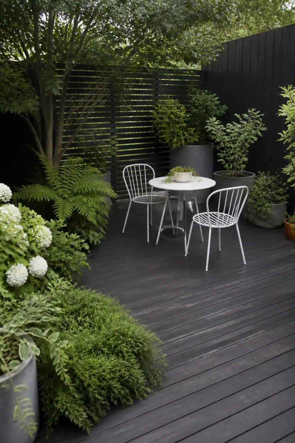 Dark gray decking with white metal bistro set in a shaded north facing garden — north facing garden ideas