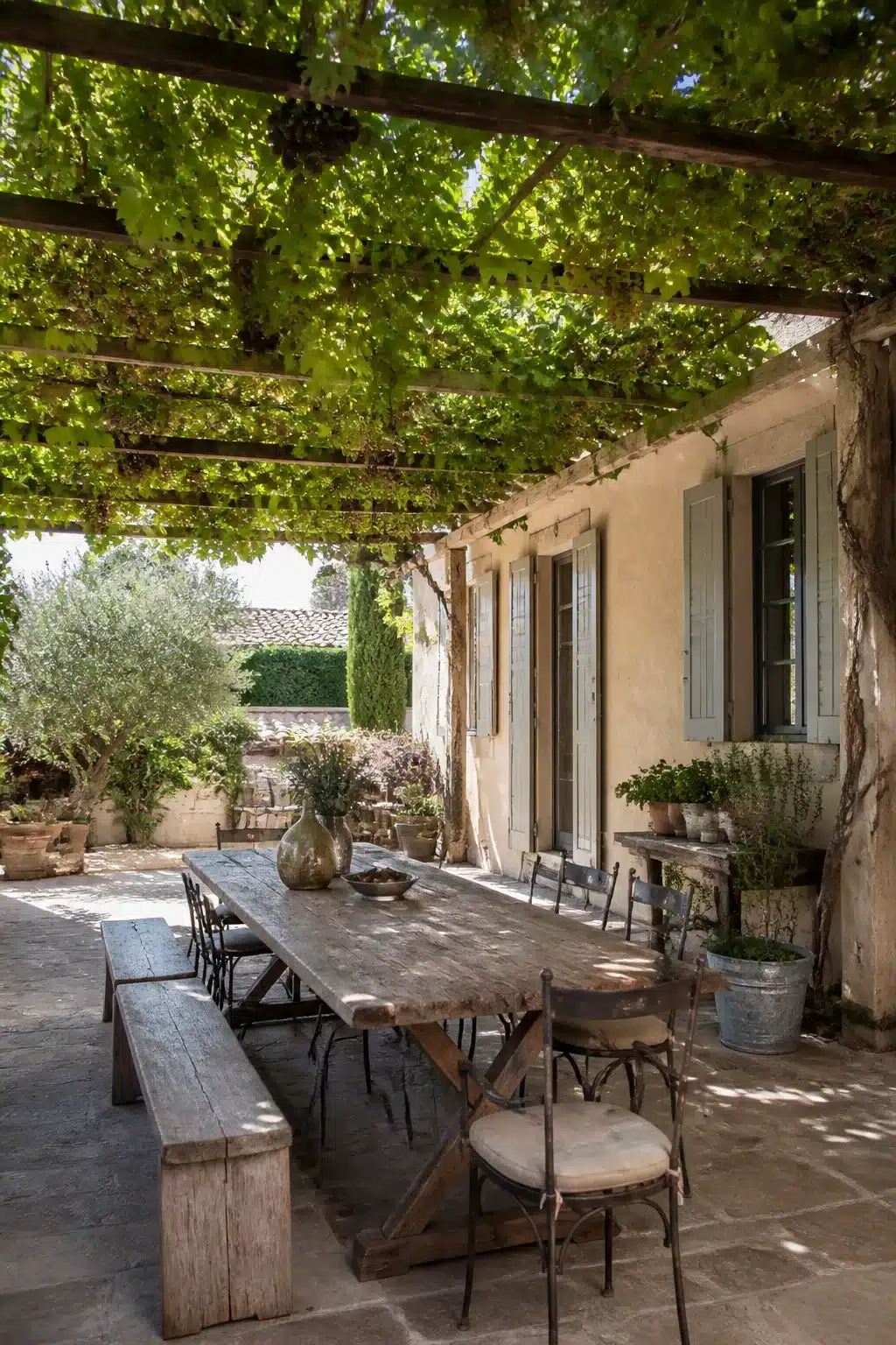 Grapevine pergola patio shade idea with rustic farm table and stone paving — outdoor dining space