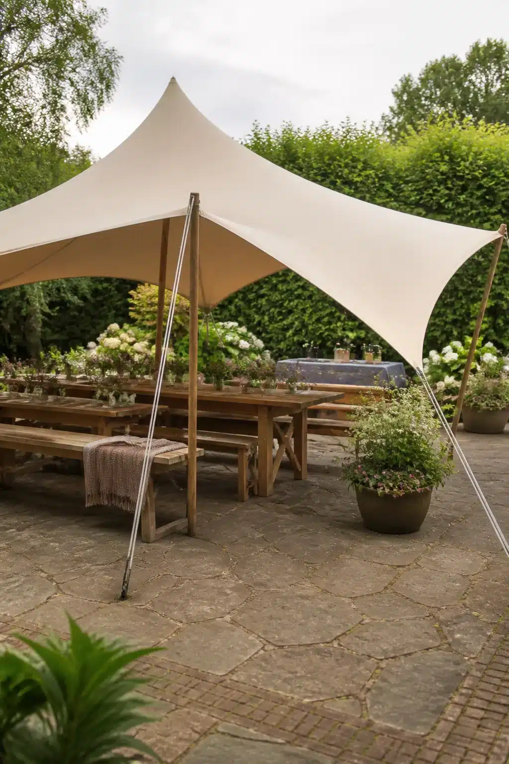 Cream canvas stretch tent over rustic timber dining benches on stone patio — patio shade ideas for entertaining