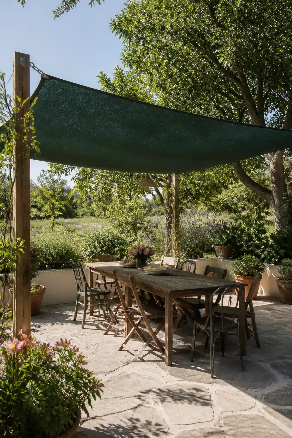 Dark green shade cloth canopy over a stone patio dining area — patio shade ideas with mismatched chairs and garden views