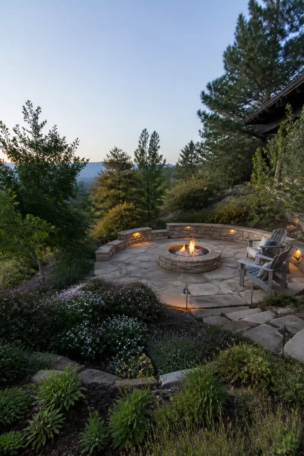 Circular stone firepit on a flagstone terrace carved into a sloped backyard — sloped backyard landscaping ideas
