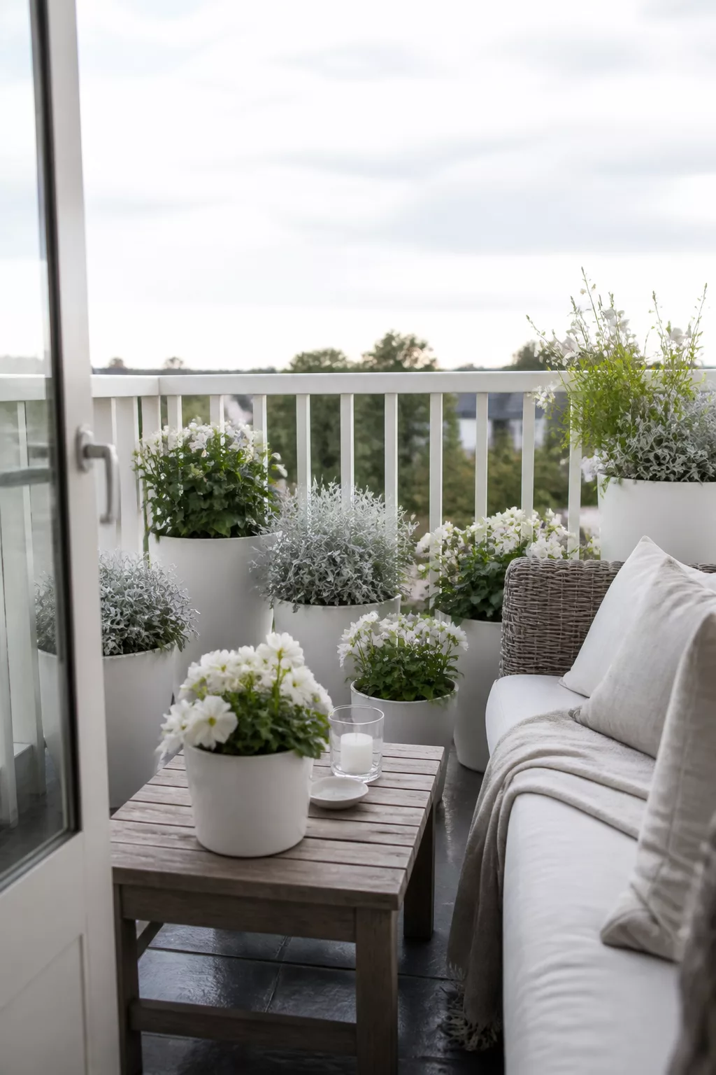 Small balcony garden with all-white pots, white blooms, and silvery foliage plants beside a linen sofa.