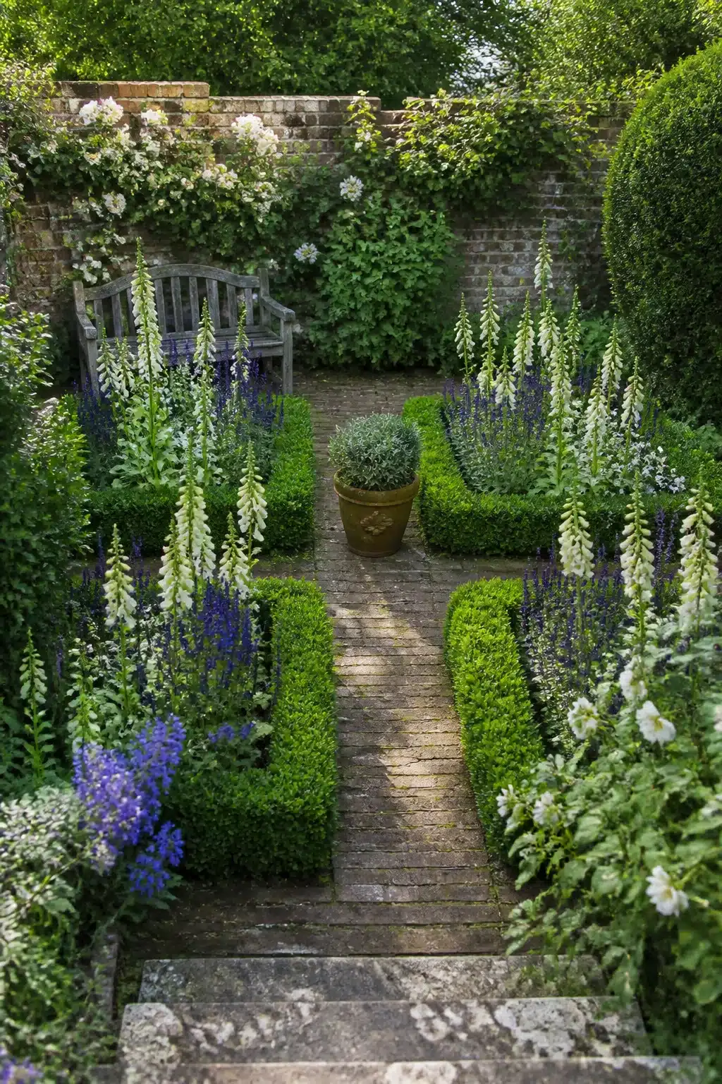Aerial view of a small English garden with box-edged formal beds, white foxgloves, blue salvia and a brick path.