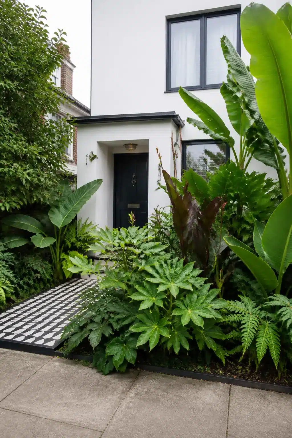 Small front garden with tropical banana plants, fatsia, and a black and white geometric tile path leading to a black front door.