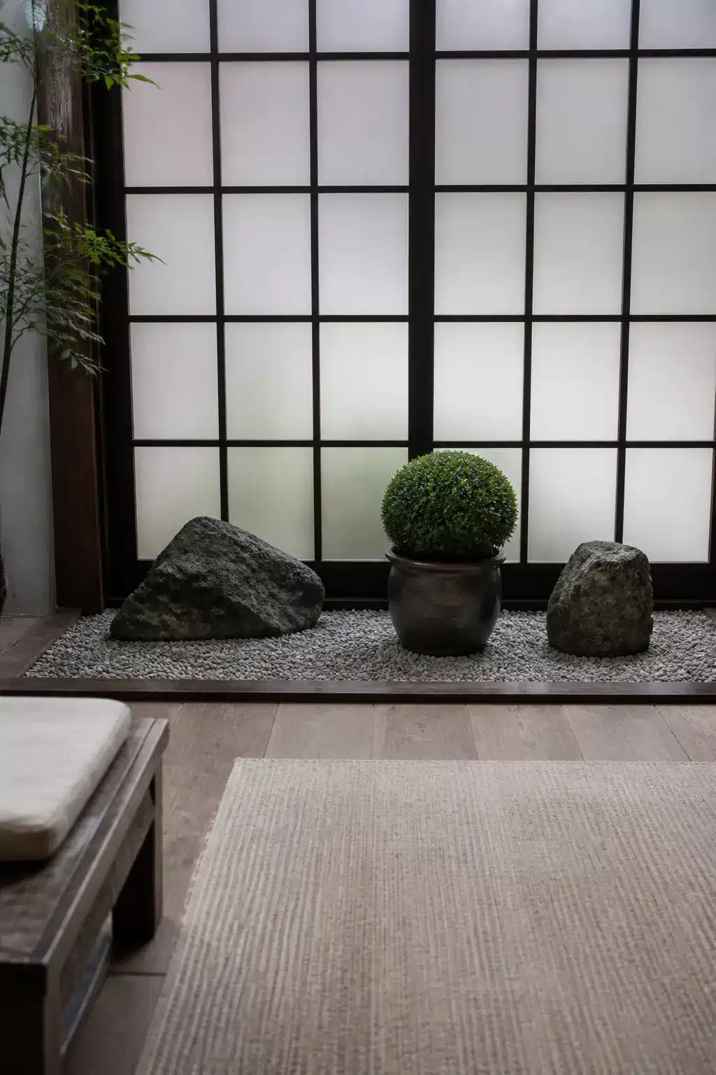 Small Japanese garden with shoji screen backdrop, raked pebbles, granite boulders, and ball topiary in a dark glazed pot.