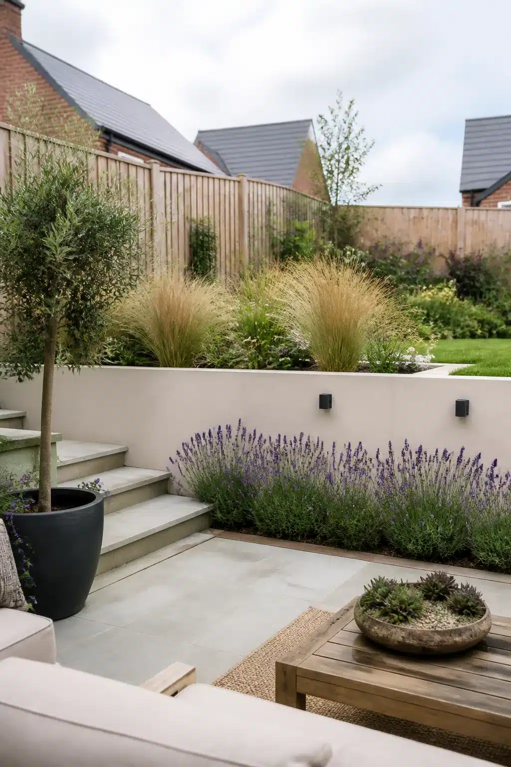 Small new build garden ideas with tiered lavender border, cream retaining wall, and ornamental grasses on sloped plot