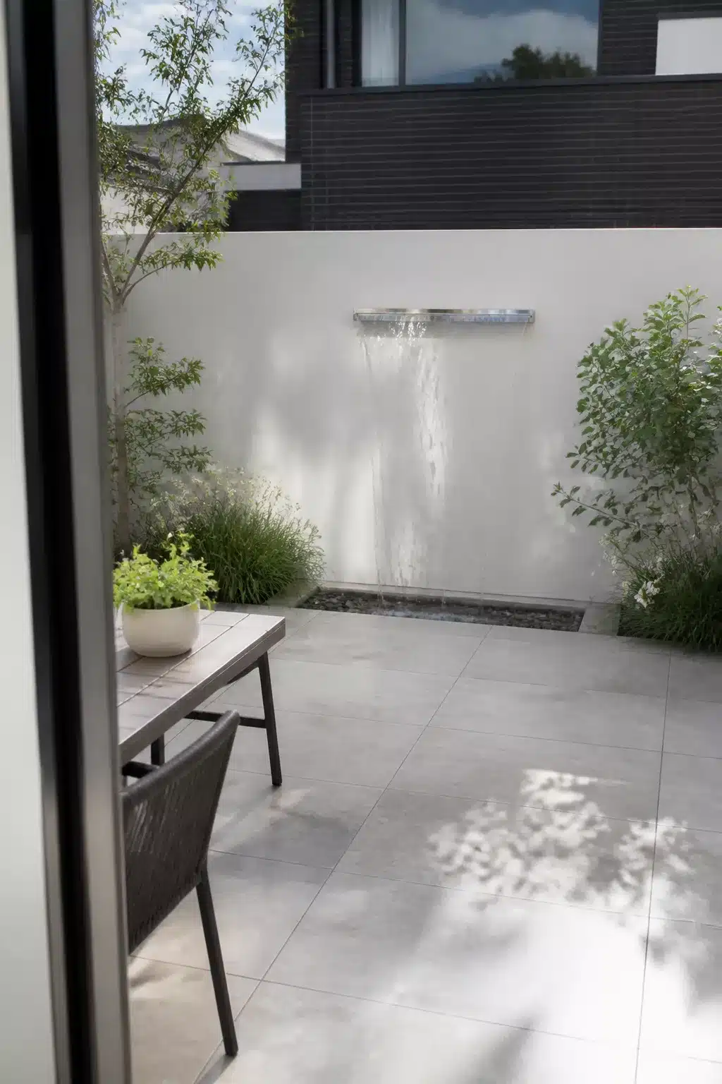 Small new build garden ideas with a stainless steel wall-mounted water blade feature and pale courtyard paving