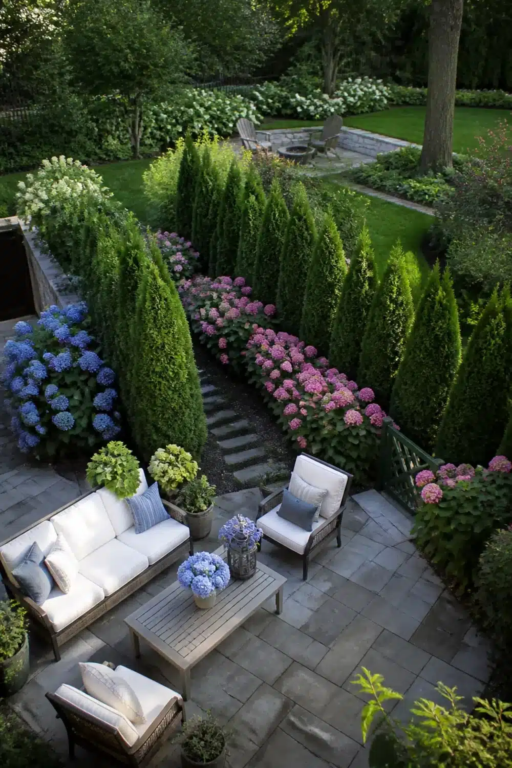 Arborvitae and hydrangea landscaping framing a stone patio with blue, pink, and white blooms as a garden room divider.