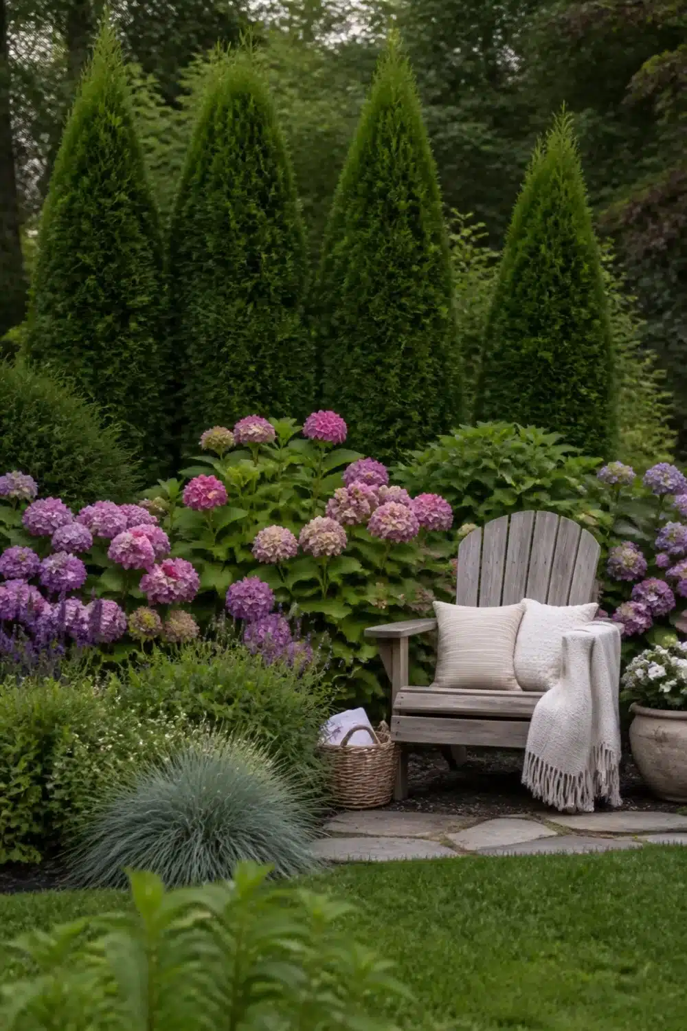 Arborvitae and hydrangea landscaping with blue fescue grass, wicker basket, and weathered Adirondack chair in mixed border.