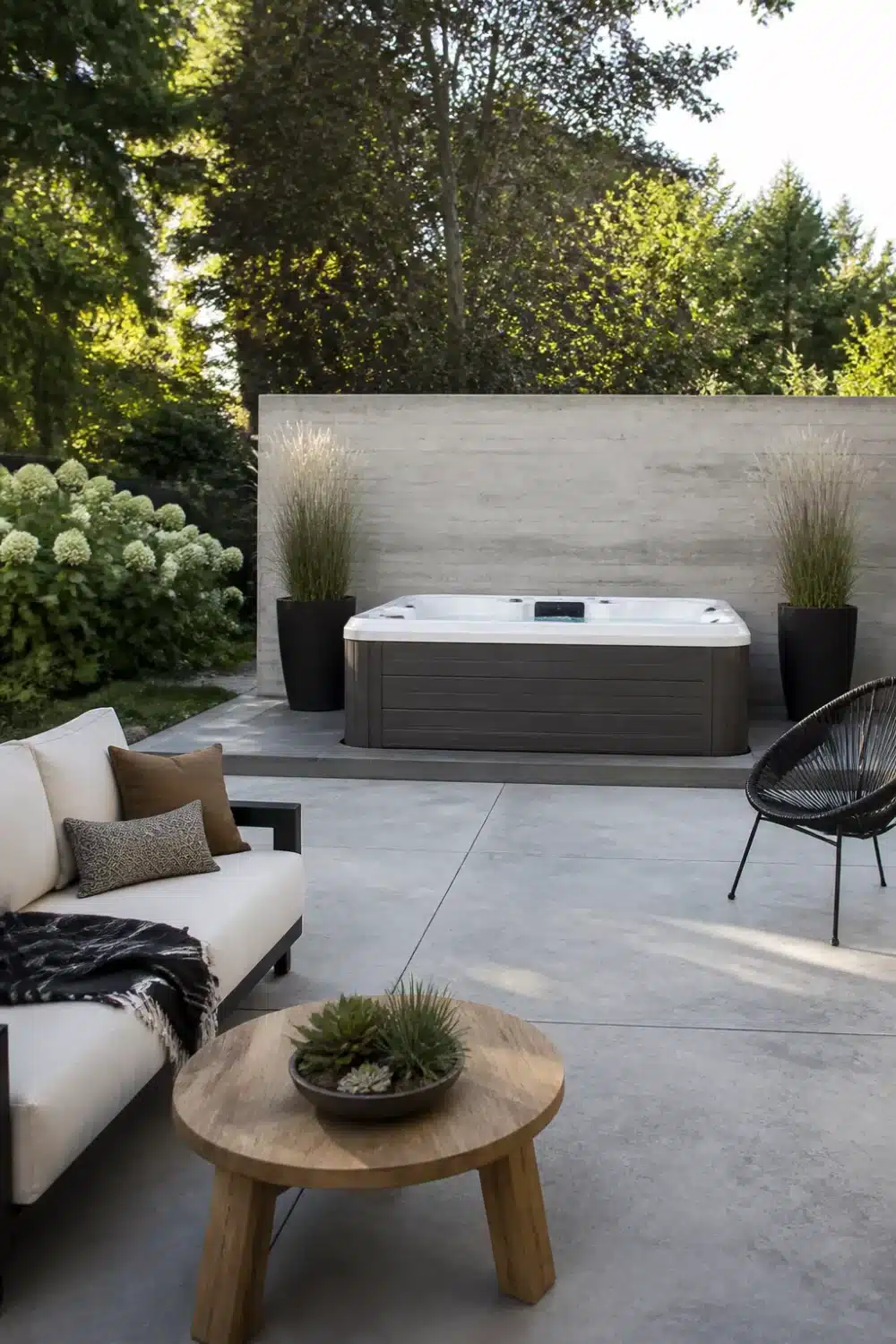 Backyard patio design with hot tub on concrete slab, poured wall backdrop, ornamental grass planters, and minimalist seating