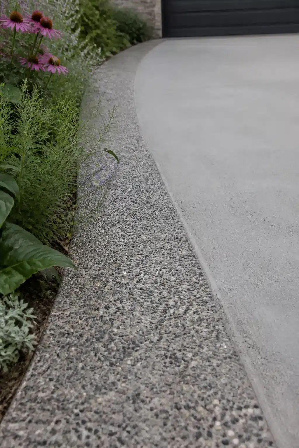 Exposed aggregate edging band alongside smooth concrete driveway with perennial planting — driveway border ideas
