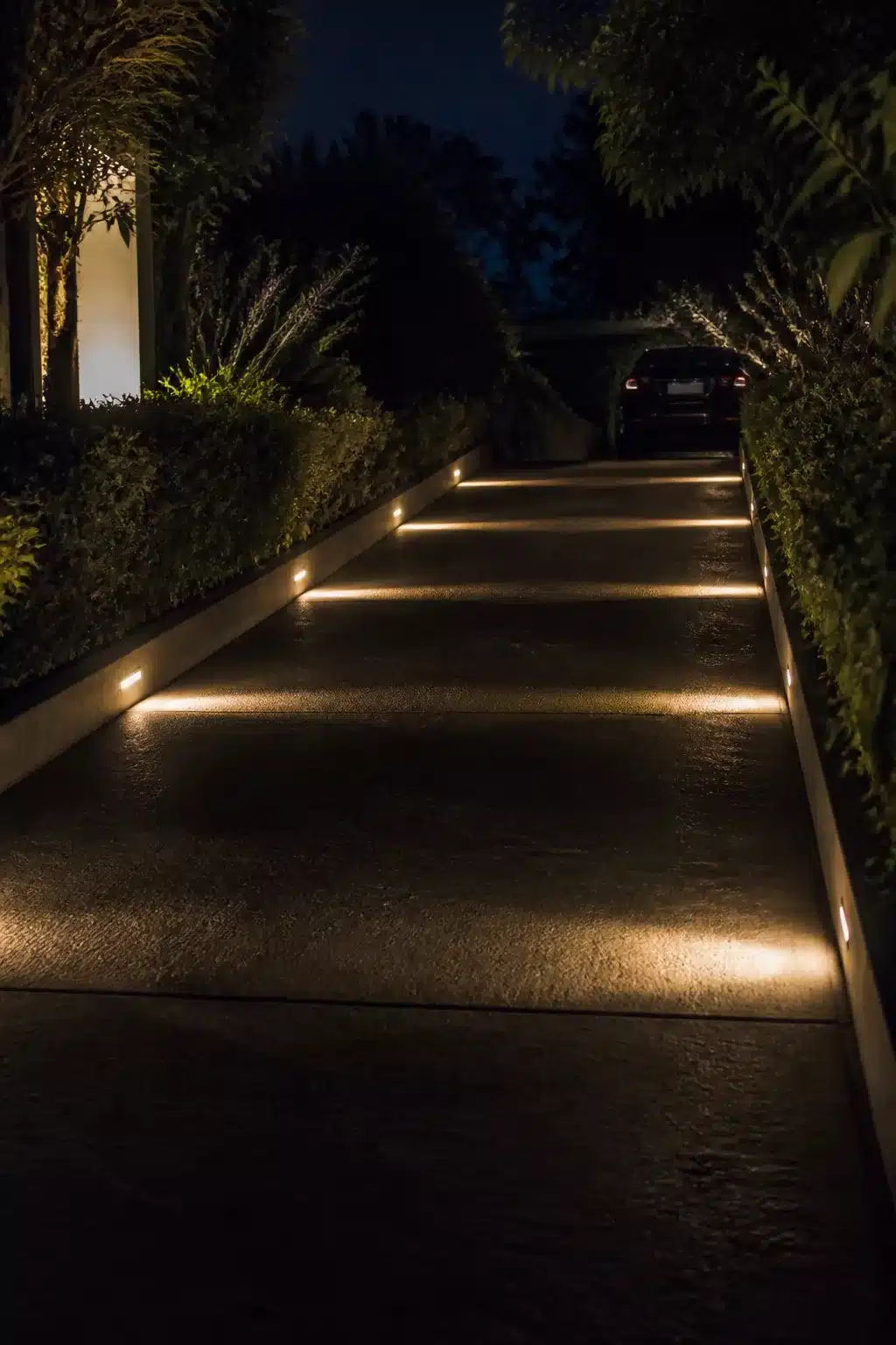 Warm step lights recessed into driveway curbing at night — driveway lighting ideas for a sloped entry