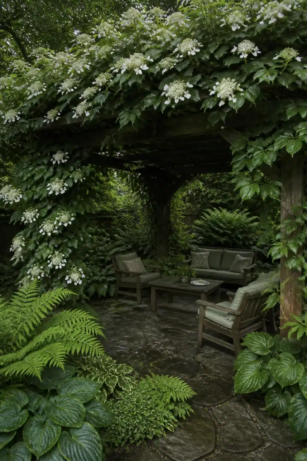 Full shade garden pergola covered in climbing hydrangea with flagstone patio, ferns, and wood seating underneath.