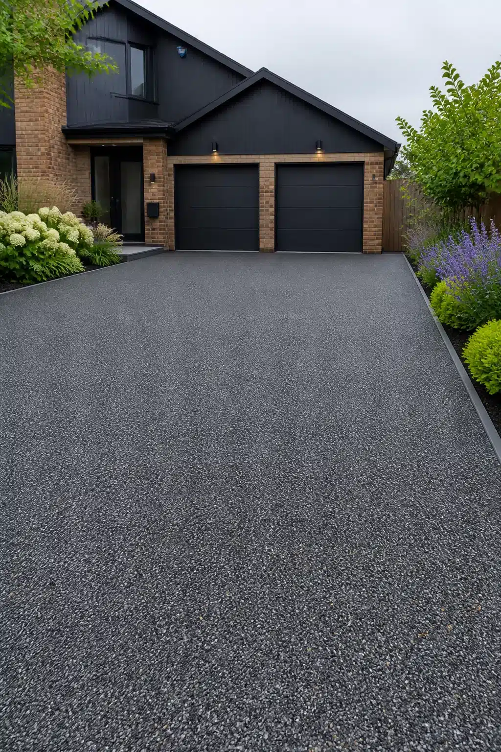 Charcoal gray resin bound aggregate driveway ideas with dark garage doors and flowering border plants