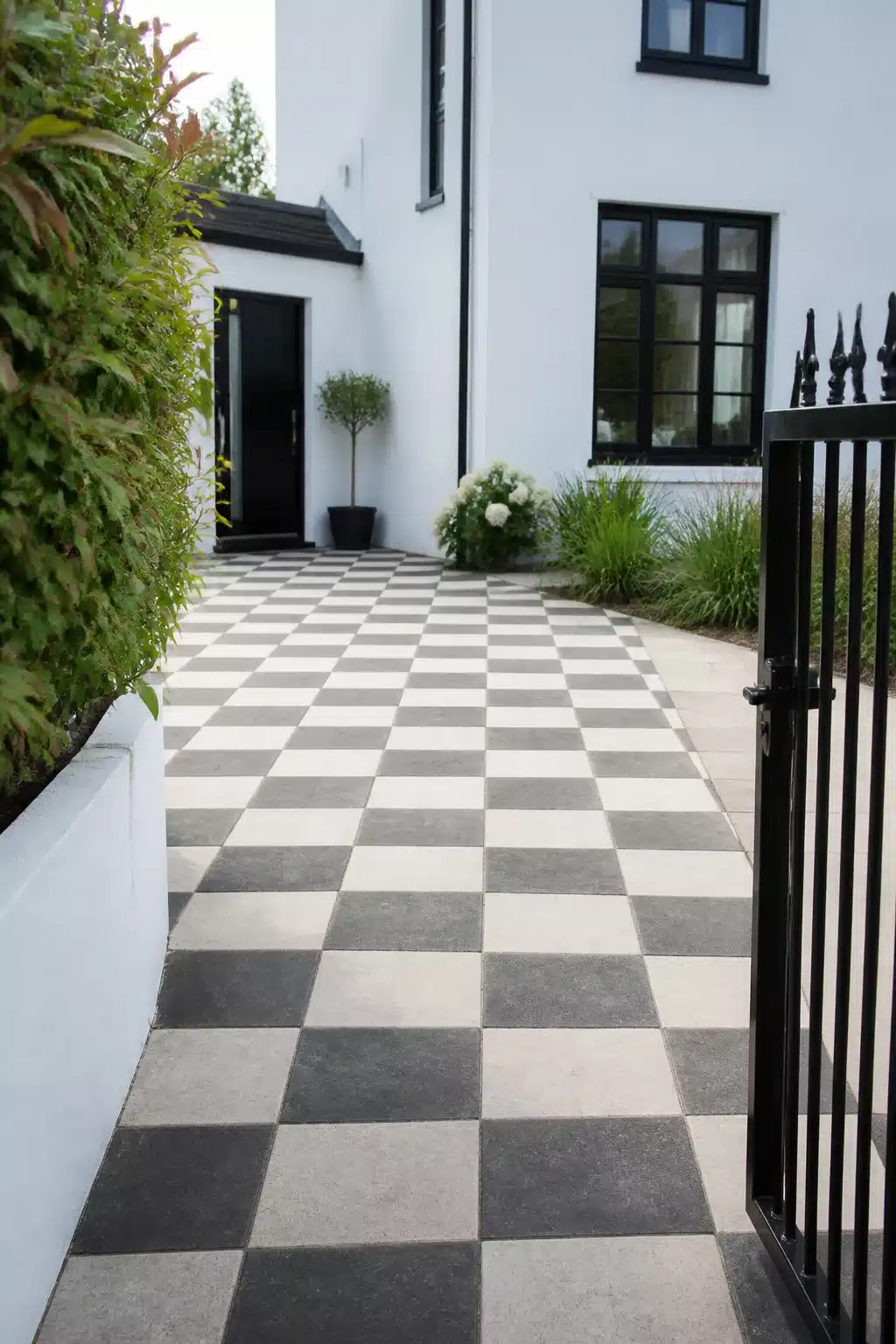 Small driveway idea with black and white checkerboard square stone paving leading to a white rendered home.