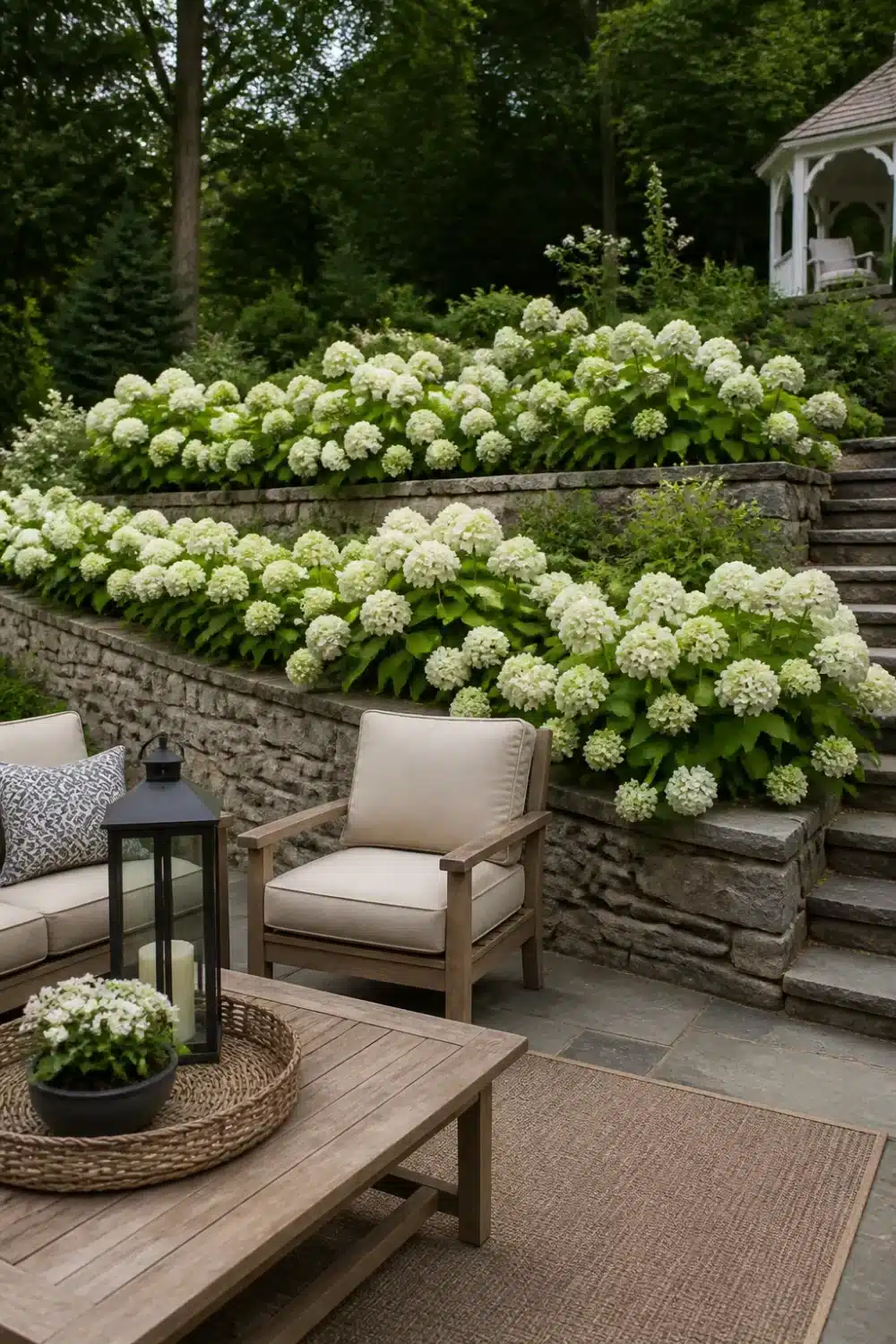 White hydrangea landscaping across stacked stone terraced retaining walls with a patio seating area below