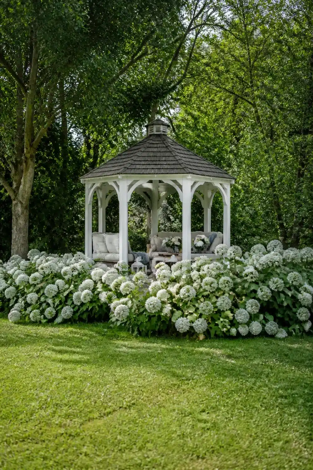 White hydrangea landscaping surrounding a white octagonal garden gazebo with lush mophead blooms and green lawn backdrop